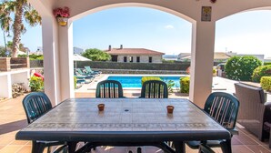 Eine überdachte Terrasse mit Tisch und Stühlen, ein Pool und Blick auf ein Gebäude mit rotem Dach.
