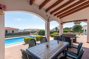 Une terrasse couverte avec une piscine, du mobilier d’extérieur et une vue sur les environs.
