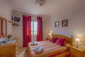 Une chambre d’hôtel comprenant un lit, un bureau avec un ordinateur, une télévision, une fenêtre avec des rideaux et une table de chevet avec une lampe.