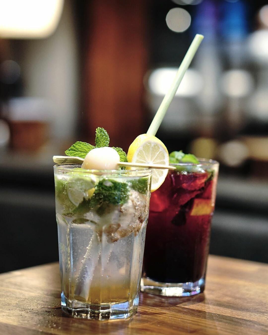 Two glasses of iced beverages with mint and lemon garnish on a wooden table.