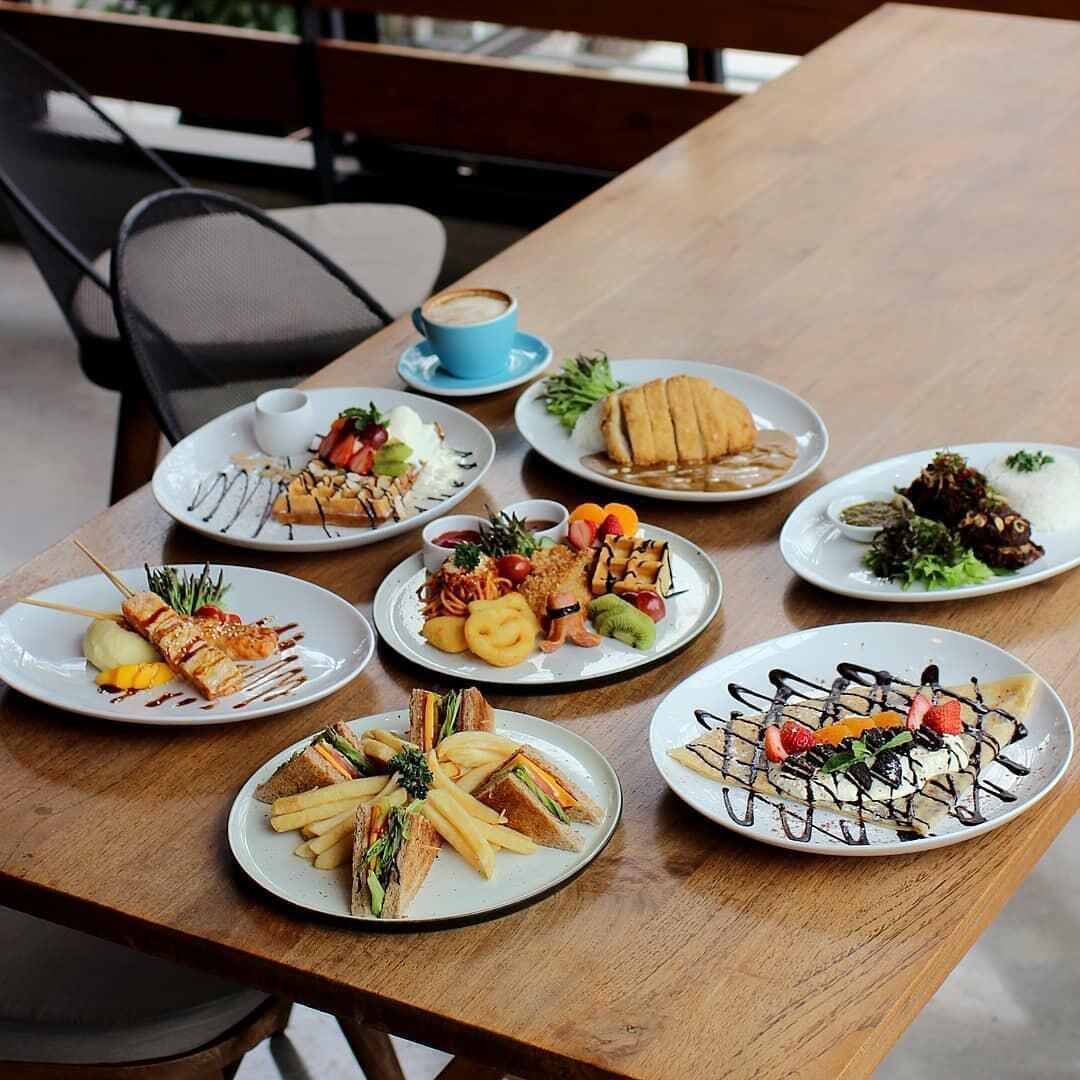 A table with various dishes including a sandwich, fries, and a dessert with fruit and chocolate.