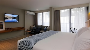 A modern hotel room with a large bed, a desk, a chair, a TV, and large windows. - Kollektiv Hotel (Bandung)