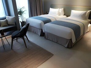 A hotel room with two beds, a seating area with a chair and table, and a view of the outdoors. - Kollektiv Hotel (Bandung)