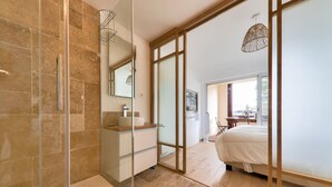 A modern bathroom with a glass shower enclosure, a vanity with a mirror, and a large bed with a white bedspread. - Sea view in Carnac, duplex for 8 (Carnac)