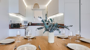 A dining table set with white plates, wine glasses, and cutlery, centered with a decorative plant in a textured pot. - Sea view in Carnac, duplex for 8 (Carnac)