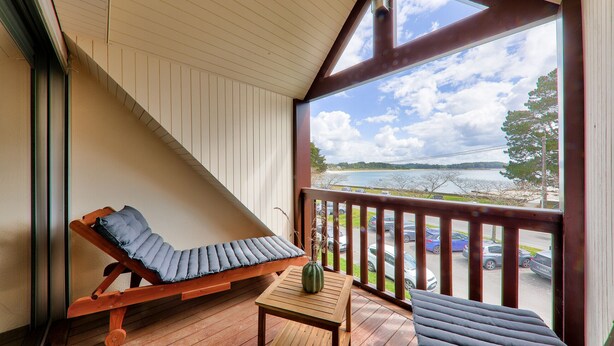 A wooden deck with a cushioned lounge chair, a small table with a vase, and a view of a parking lot and trees. - Sea view in Carnac, duplex for 8 (Carnac)