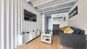 A modern living room with a grey sofa, white console, and a flat-screen TV mounted on a white wall. - Sea view in Carnac, duplex for 8 (Carnac)