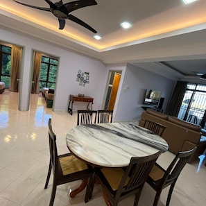 A dining area with a round table and chairs, a ceiling fan, recessed lighting, and a view through large windows.