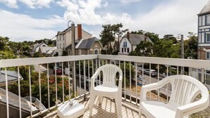 Een balkon met witte stoelen, uitzicht op een straat met huizen en een heldere lucht.