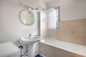 A bathroom with a white sink, a round mirror, and a glass-enclosed shower.