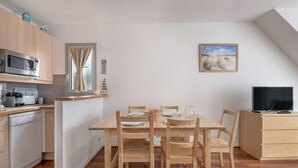 Een praktische keuken met een magnetron, broodrooster en vaatwasser. Er is een eettafel met stoelen en een televisie op een kast.