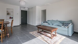 A modern living room with a light blue sofa, a wooden coffee table, and a dining area with a wooden table and chairs. - New home for 4 adults - 2 children - Garden (Piriac-sur-Mer)