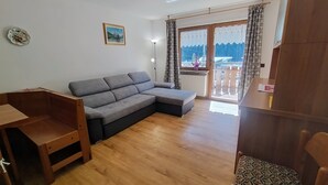 Un salón con un sofá seccional gris, una mesa de madera, un radiador y vistas a través de una ventana con cortinas.