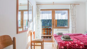Un dormitorio con cama, una silla, una ventana con cortinas y vistas al exterior.