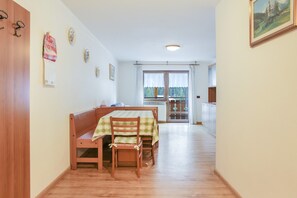 Un coin repas avec un banc et une table en bois, une cuisine à l’arrière-plan et une vue par la fenêtre.