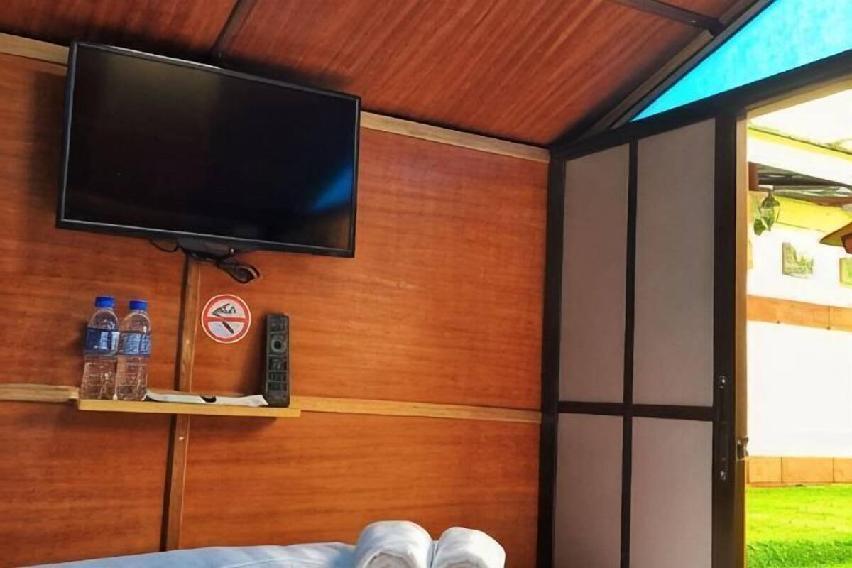 Habitación con televisión, botellas de agua, un control remoto y una puerta que da a un espacio exterior.