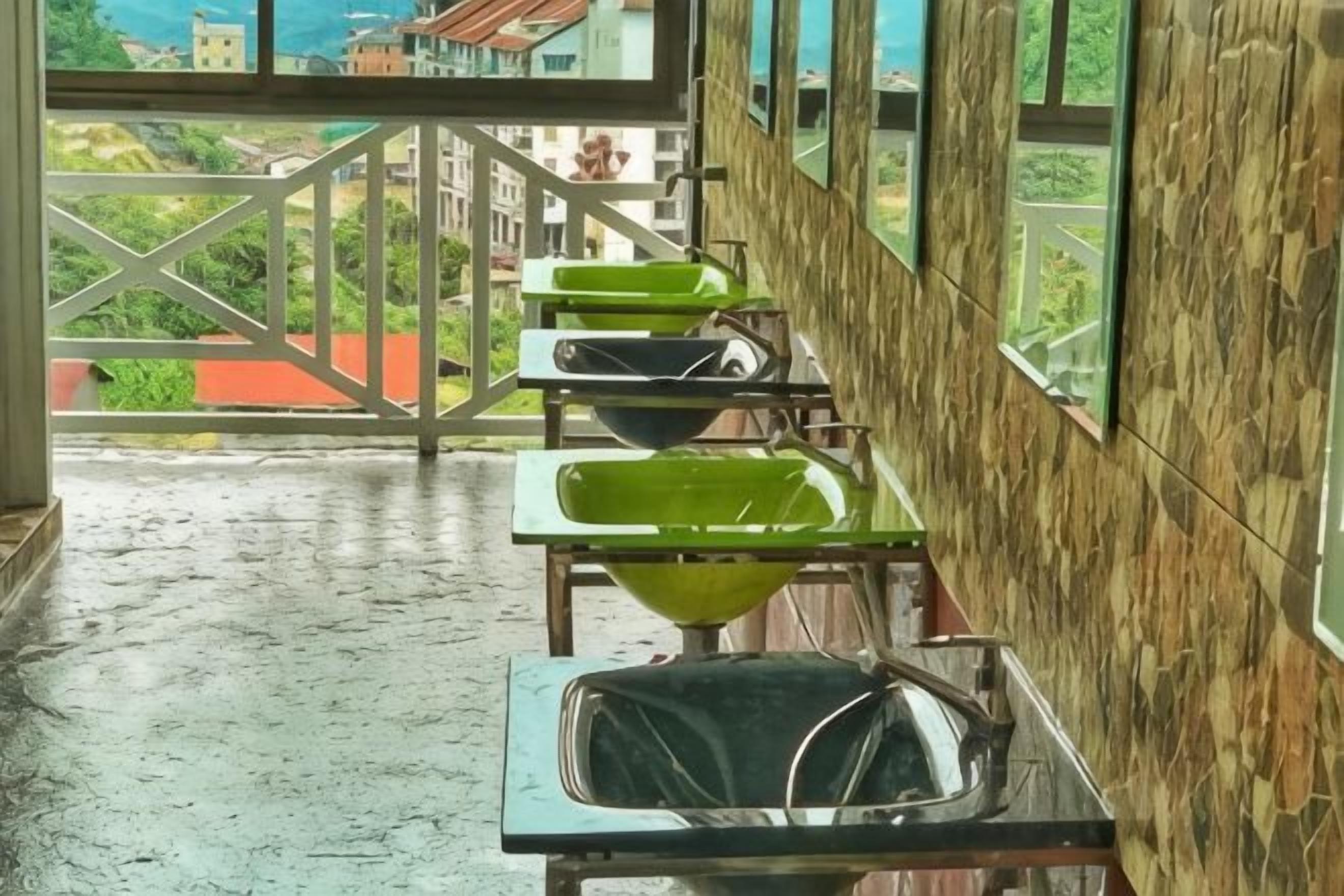 A row of sinks with green basins in a room with wooden walls and a view of greenery outside.