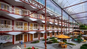 A hotel with multiple balconies, a central courtyard with seating, and a greenhouse structure. - Kea Garden Mini Chalet (Brinchang)