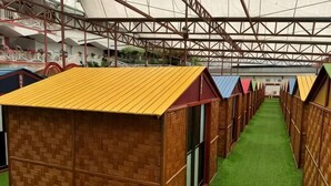 A row of wooden cabins with a green artificial turf floor and a metal roof structure. - Kea Garden Mini Chalet (Brinchang)