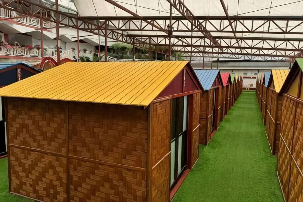 Una fila de cabañas de madera con piso de césped artificial verde y estructura de techo metálica.