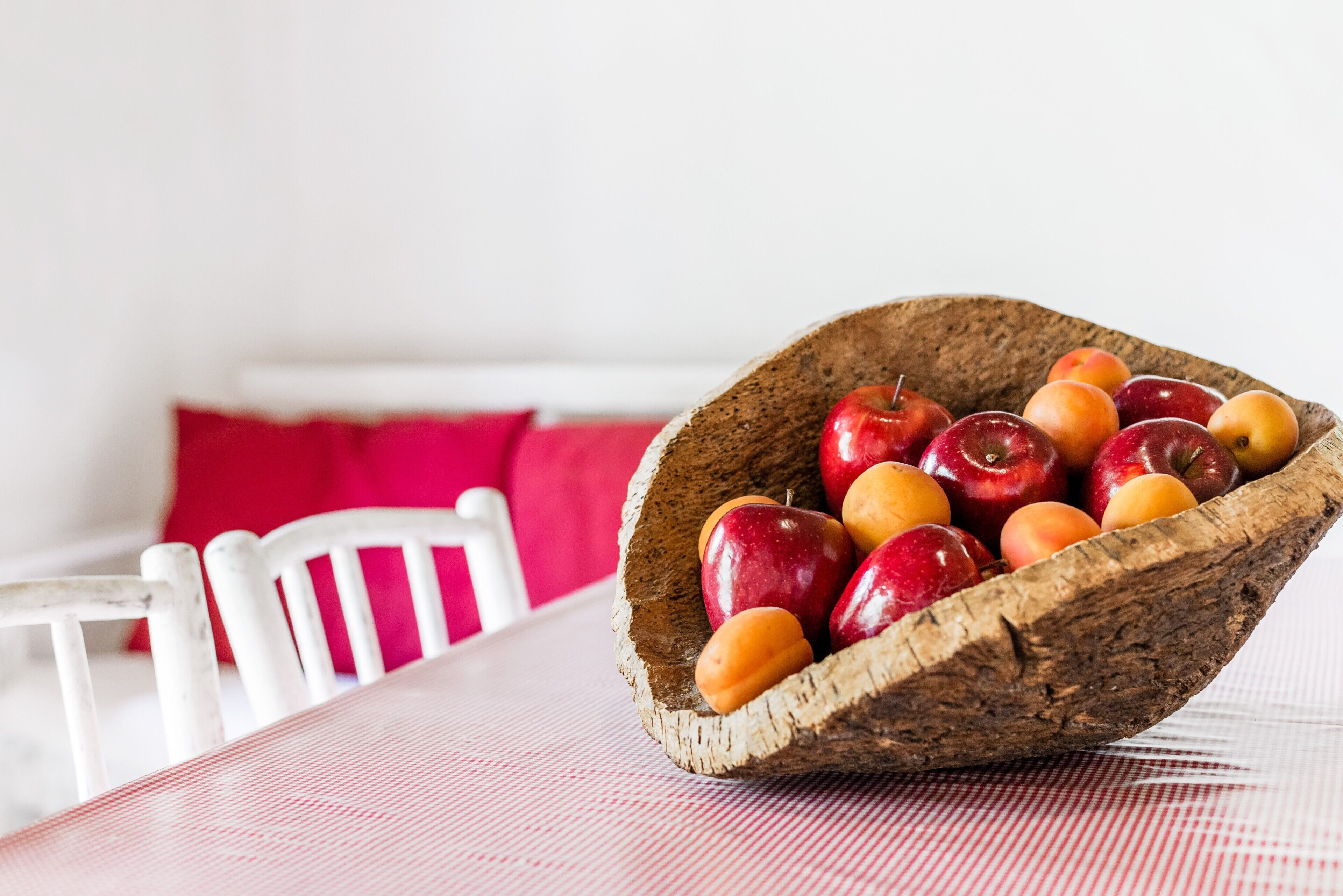 Un saladier en bois rempli de pommes et d’abricots, posé sur une table recouverte d’une nappe à carreaux rouges et blancs.