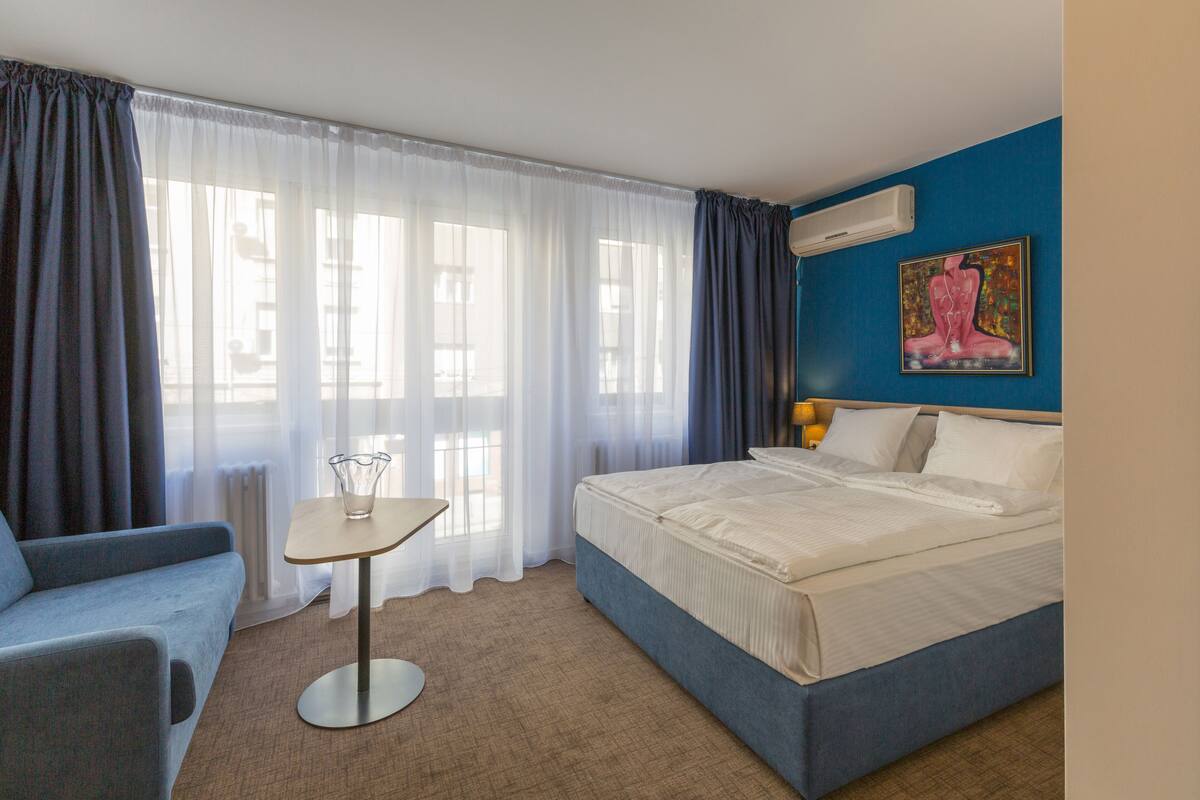 Una habitación de hotel con una cama, una mesita, una silla y un cuadro en la pared.
