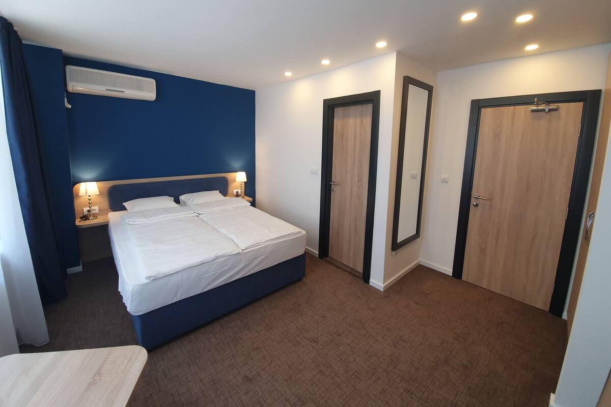 Una habitación de hotel con una cama grande, lámparas de noche, un armario y un espejo.