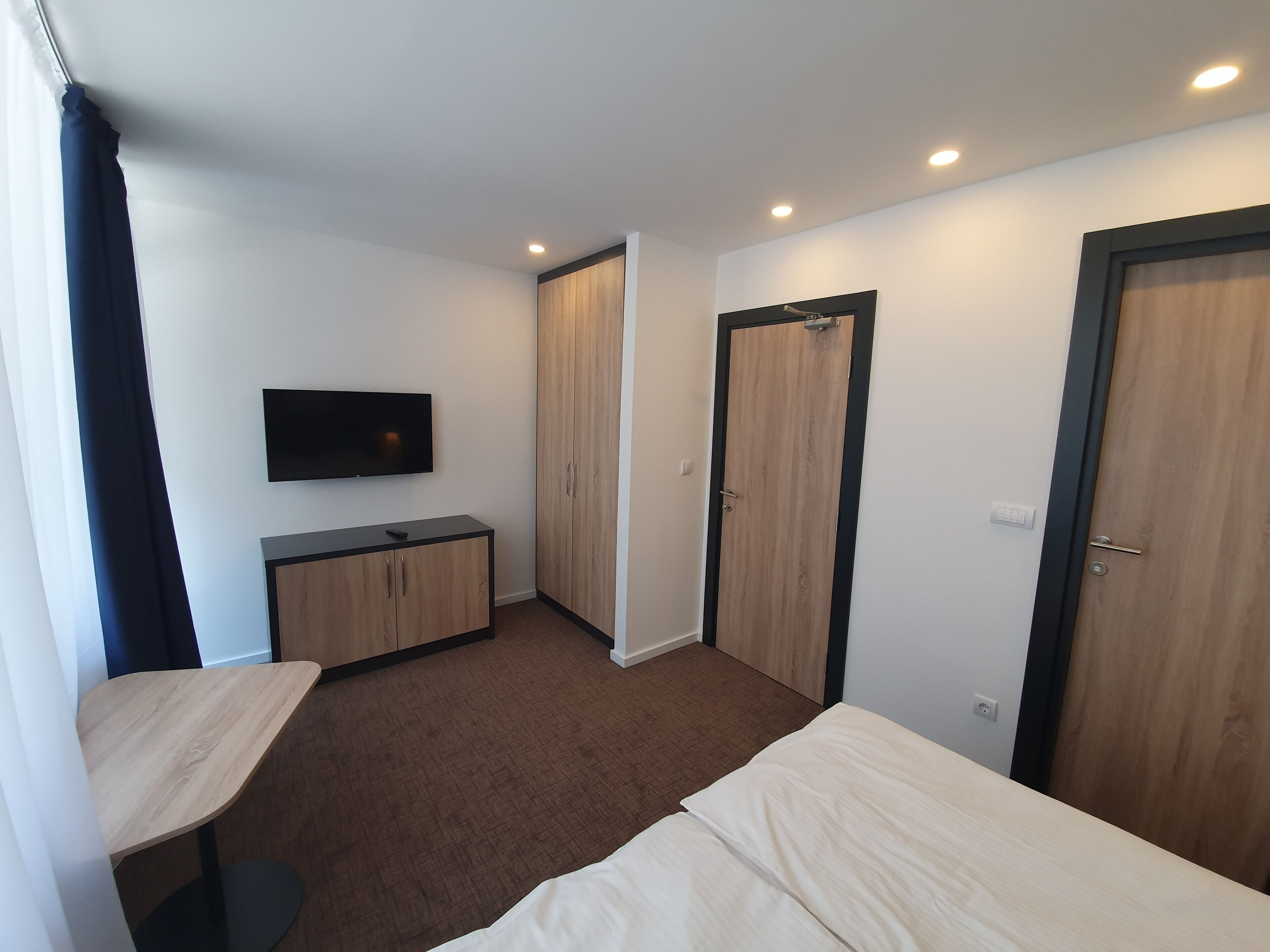 Un dormitorio con cama, televisor montado en la pared, armario y escritorio.