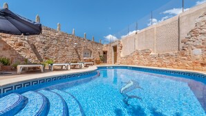 En swimmingpool med stenvægge, en bænk og en parasol.