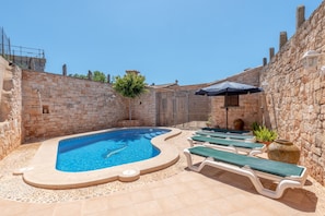 A swimming pool with lounge chairs and a stone wall.