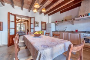 A dining area with a table set for four, wooden chairs, a chandelier, and a kitchen with cabinets and appliances.