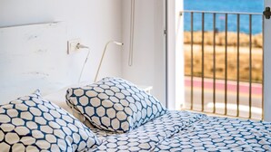 Een bed met beddengoed met patroon, een stopcontact en uitzicht op de zee door een balkonhek.