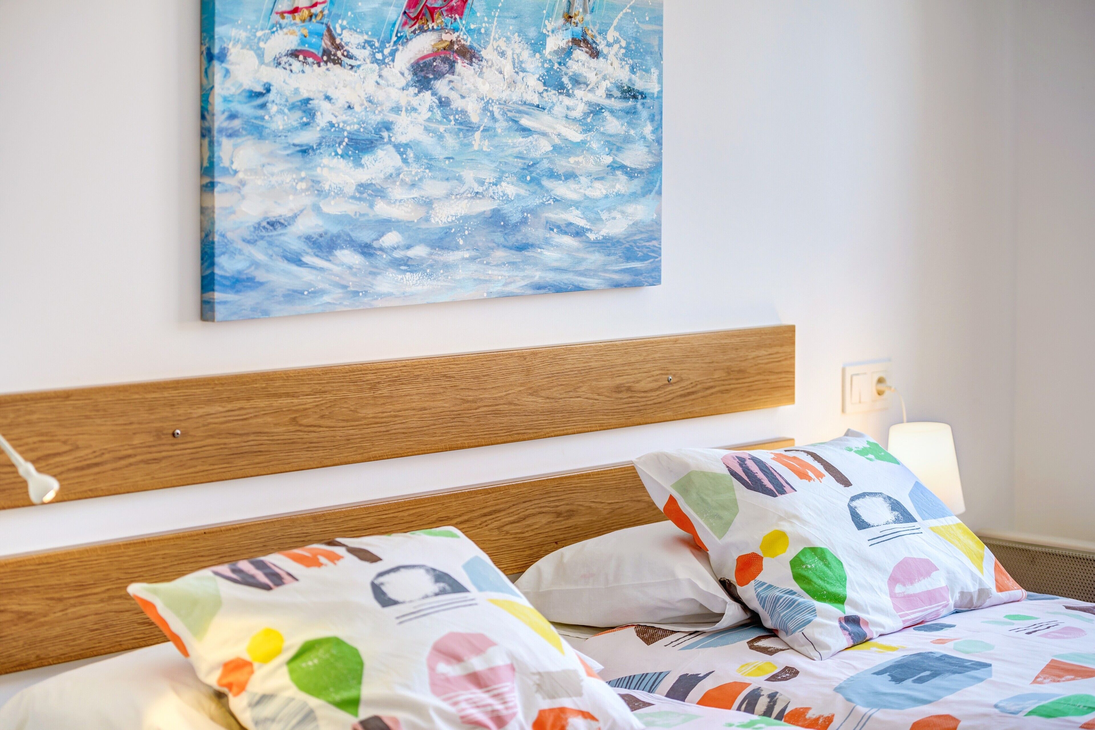 Un lit avec des oreillers aux couleurs vives et un tableau représentant un paysage enneigé accroché au mur.