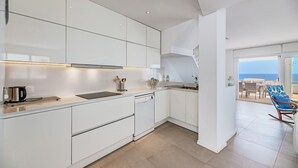 Een moderne keuken met witte kastjes, een vaatwasser en uitzicht op zee door een groot raam.