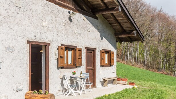 Un bâtiment rustique avec une façade en pierre, des volets en bois et un petit espace extérieur aménagé avec des chaises et une table.