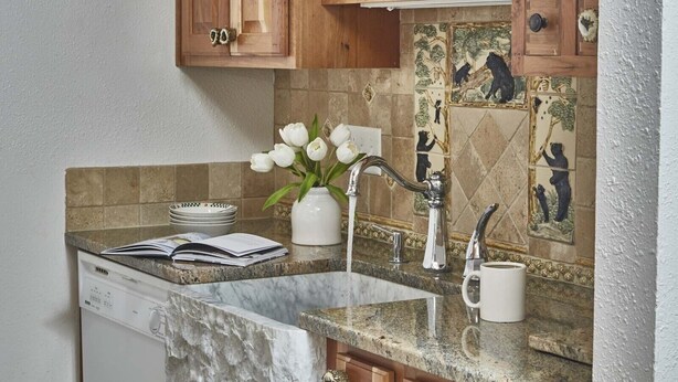 A kitchen with wooden cabinets, a marble countertop, a sink with a modern faucet, and a vase with white flowers. - JHRL - Gros Ventre B10 - Cozy mountain condo (Teton Village)