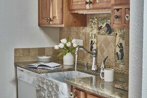 A kitchen with wooden cabinets, a marble countertop, a sink with a modern faucet, and a vase with white flowers.