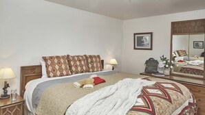 A hotel room with a large bed, a nightstand with a lamp, a dresser, and a mirror reflecting the room. - JHRL - Gros Ventre B10 - Cozy mountain condo (Teton Village)