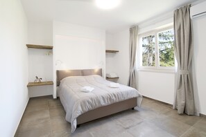 A bedroom with a bed, a bedside table, a window with curtains, and a view of trees.