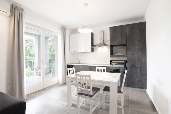 A modern kitchen with white cabinetry, a dining table with chairs, and a large window with a view of greenery.