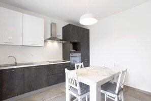 A modern kitchen with a white countertop, dark cabinets, and a dining table with chairs.