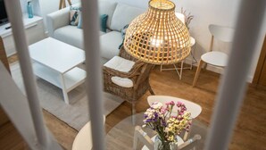 A modern living room with a white sofa, a wicker chair, a glass coffee table with a vase of flowers, and a hanging lamp. - Duplex Flamingo Cadiz (Cádiz)