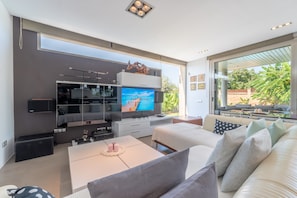 Una sala moderna con un televisor grande, un sofá, una mesa de centro y una zona de comedor.
