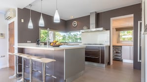 Una cucina moderna con isola centrale, sgabelli da bar, lampade a sospensione e vista sul verde.