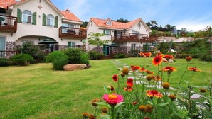 A residential area with two houses featuring balconies, a well-maintained lawn, and flowering plants.