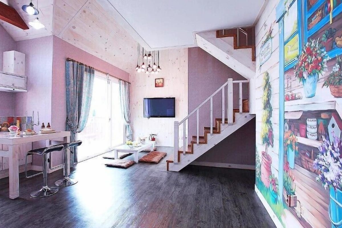 A modern kitchen with a dining area, a staircase, and a mural.