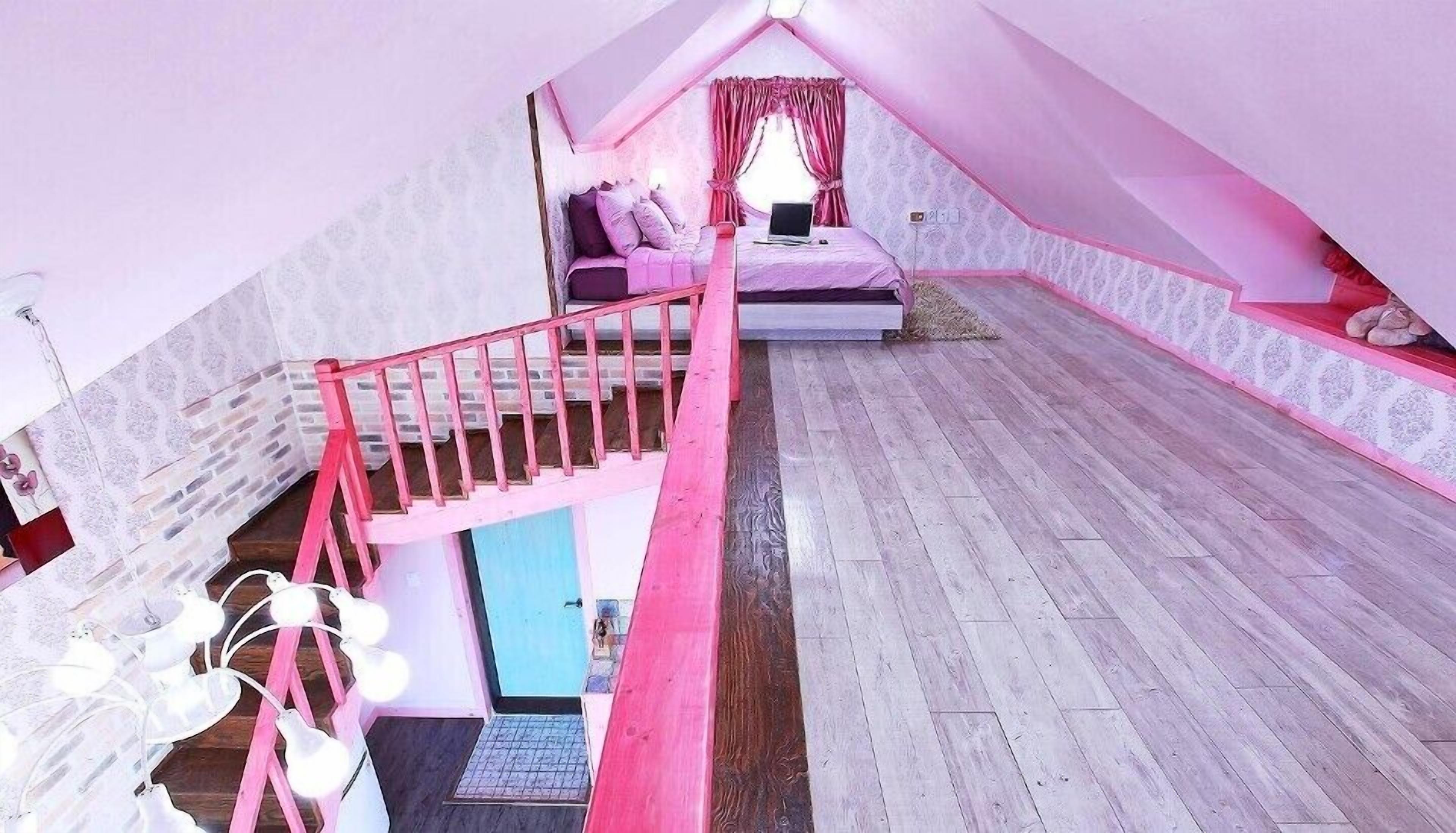 A pink-themed attic bedroom with a wooden floor, a staircase, and a bed with a laptop.