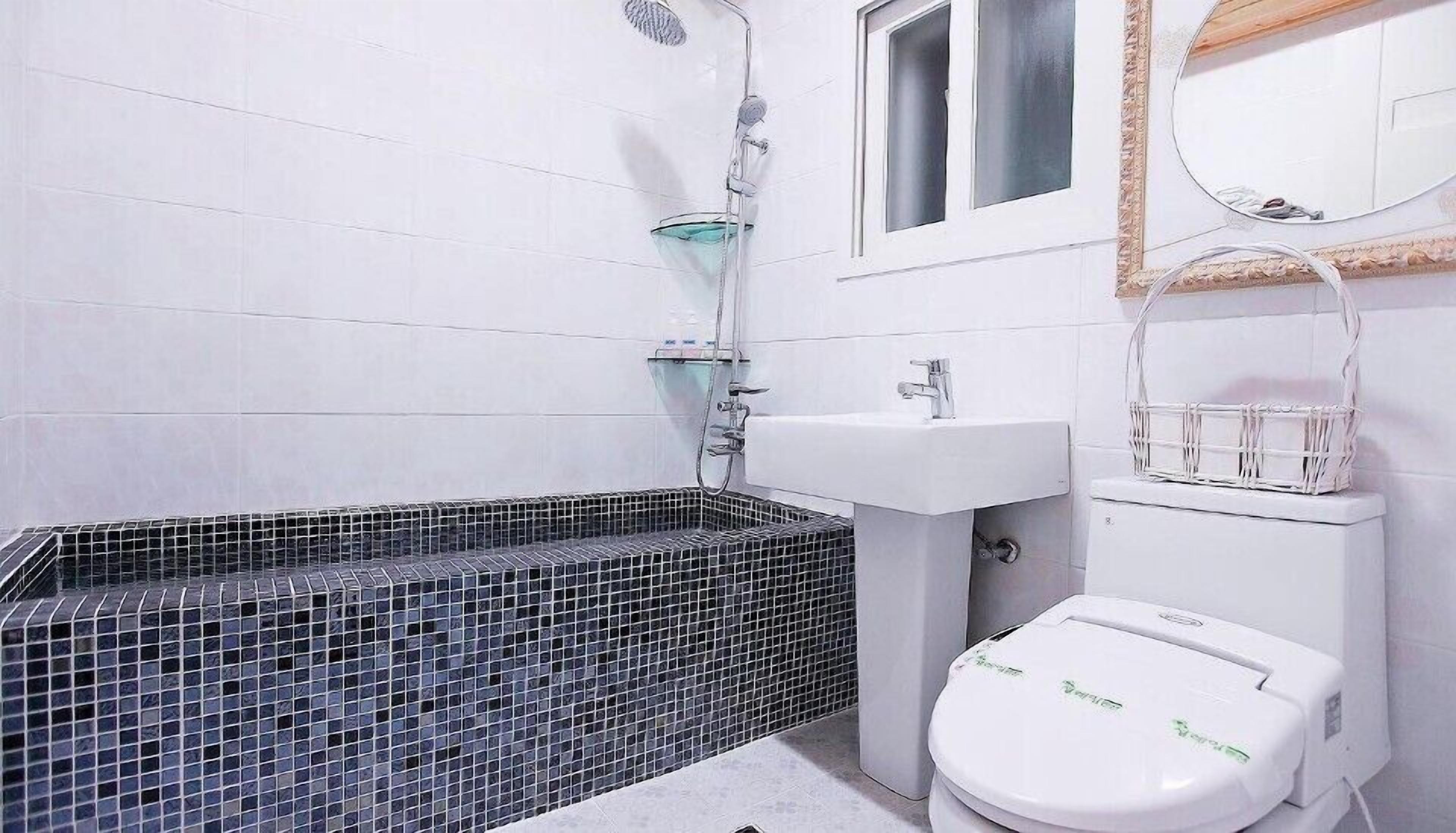 A bathroom with a black-tiled bathtub, a white sink, and a toilet.