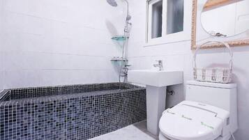 A bathroom with a black-tiled bathtub, a white sink, and a toilet.