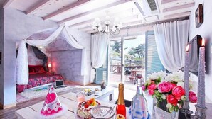 Un dormitorio con cama a dosel, una zona de comedor con mesa dispuesta para una comida, y un balcón con vistas.
